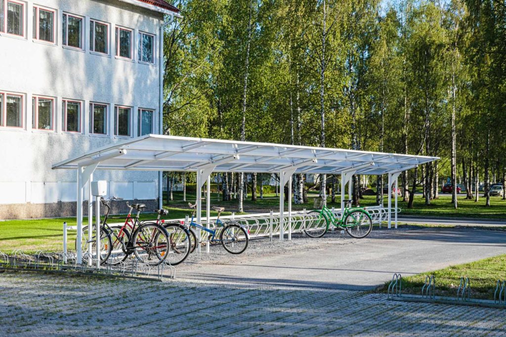 Valkoinen pyöräkatos koivujen vieressä