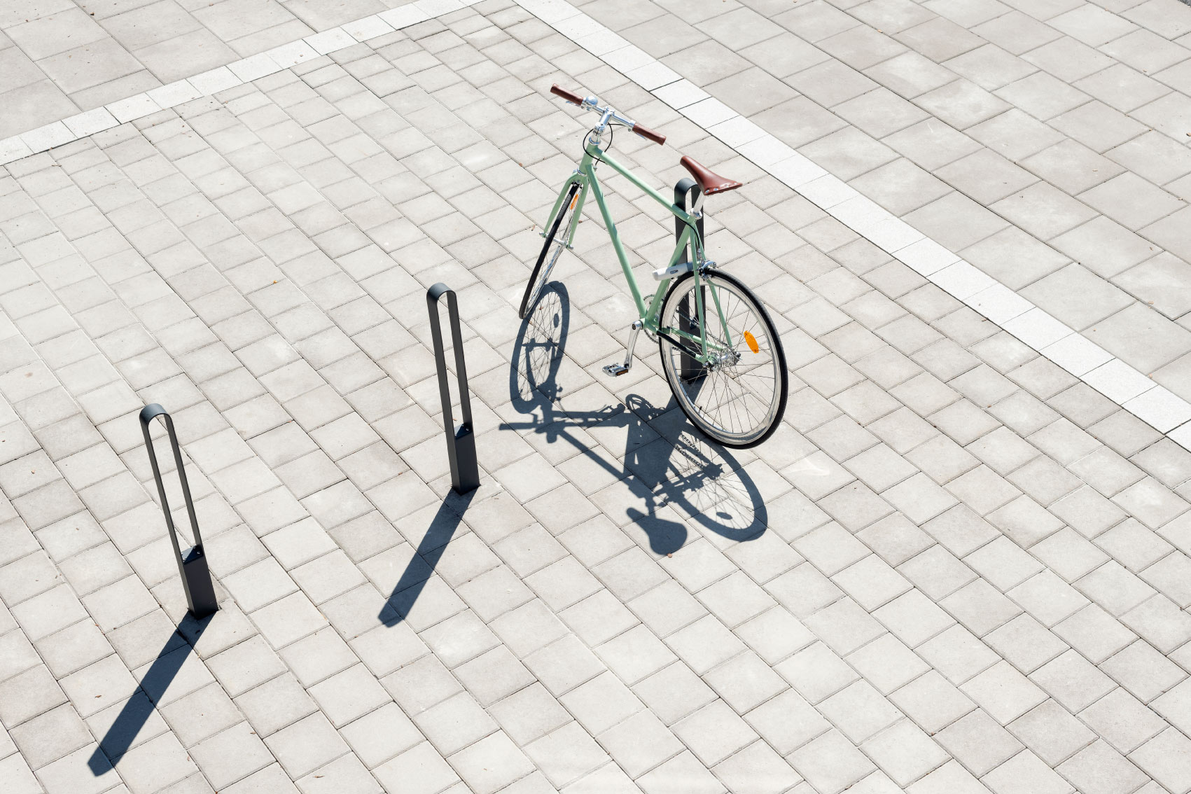 Cykel med sadel i läder parkerad och låst vid en av tre cykelpollare LUX från Cyklos