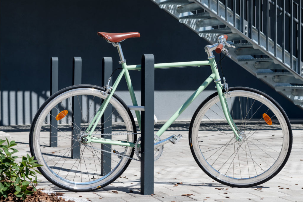 Fyra cykelpollare LUX för offentlig miljö där det vid en av pollarna står en grön cykel