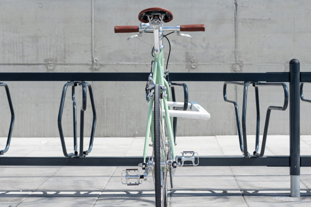 Grön cykel som står i ett svart DELTA cykelställ för offentlig miljö