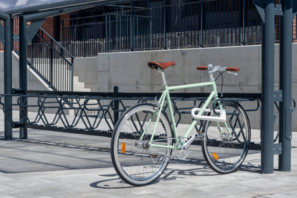 Grön cykel som är fastlåst i ramen i ett svart DELTA cykelställ för offentlig miljö
