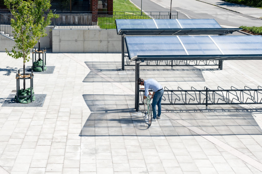 En cyklist låser sin cykel i det dubbelsidiga cykelstället DELTA under det dubbelsidiga cykeltaket YPSILON från Cyklos