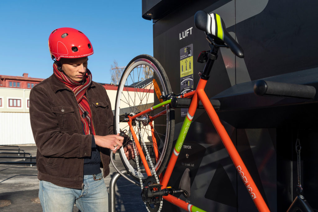 En cyklist i röd hjälm fäster pumpmunstycket för att pumpa cykeln på cykelservicestationen GRAND från Cyklos