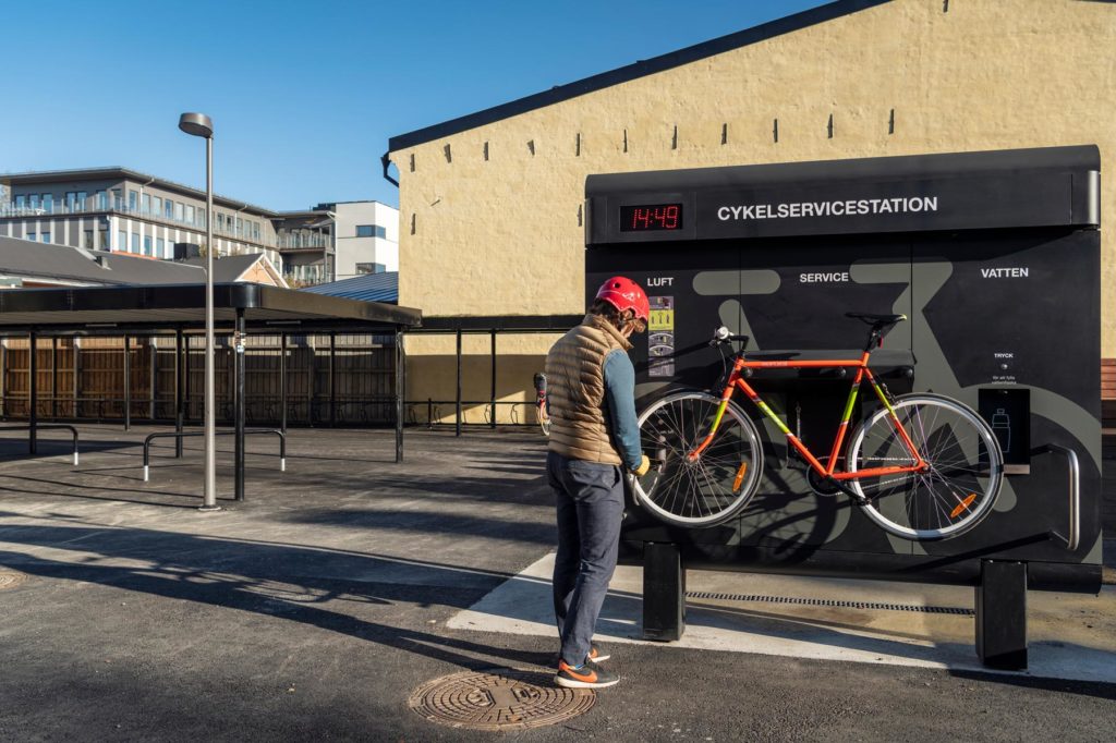 En cyklist pumpar däcken på sin rödgröna cykeln som är upphängd på cykelservicestationen GRAND från Cyklos