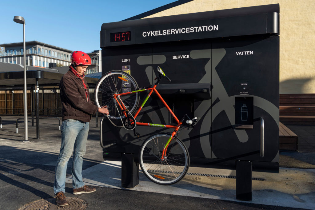 En cyklist i röd hjälm pumpar sin rödgröna cykeln som är upphängd på cykelservicestationen GRAND från Cyklos