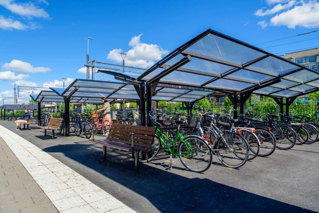 Dubbelsidigt cykeltak där en kvinna parkerar en cykel och en man sitter på en bänk.