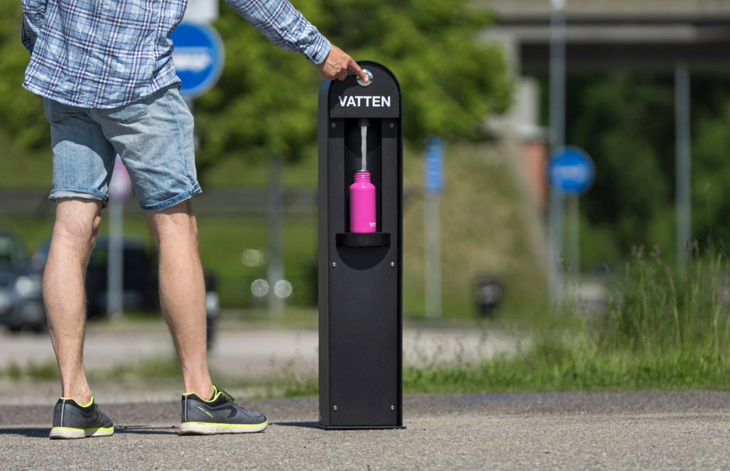 Vattenstation med rosa flaska på sommaren i offentlig miljö